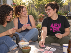 lifestyle mockup of young adult friends playing cards on a sunny patio, with a woman wearing the black 4 Ever tee and its magenta front artwork.