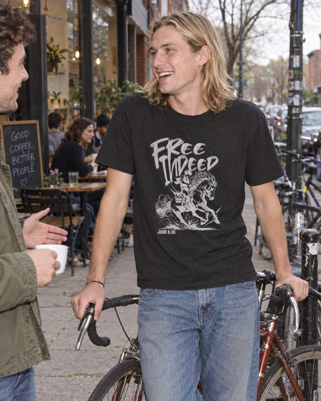 lifestyle mockup of an adult at a cafe bicycle stop wearing the black heather Free Indeed tee, with its horse and rider front artwork and John 8:36 visible.