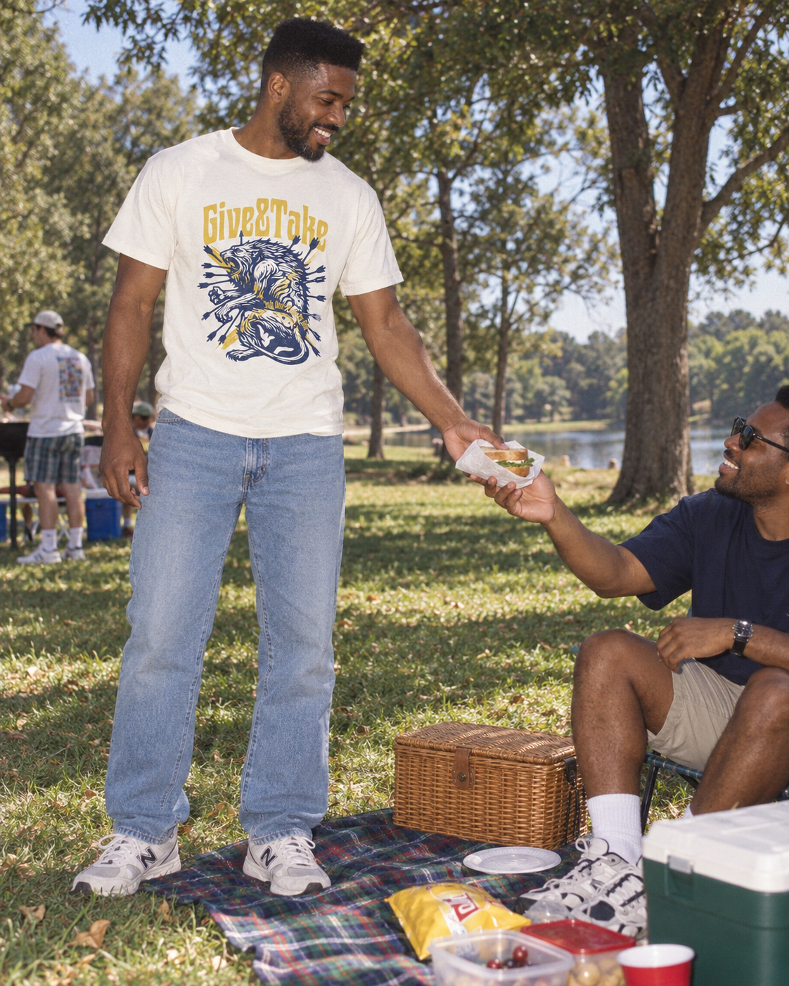 lifestyle mockup of an adult sharing a sandwich at a park picnic in the vintage white Give and Take tee, with its navy and yellow lion front artwork visible.