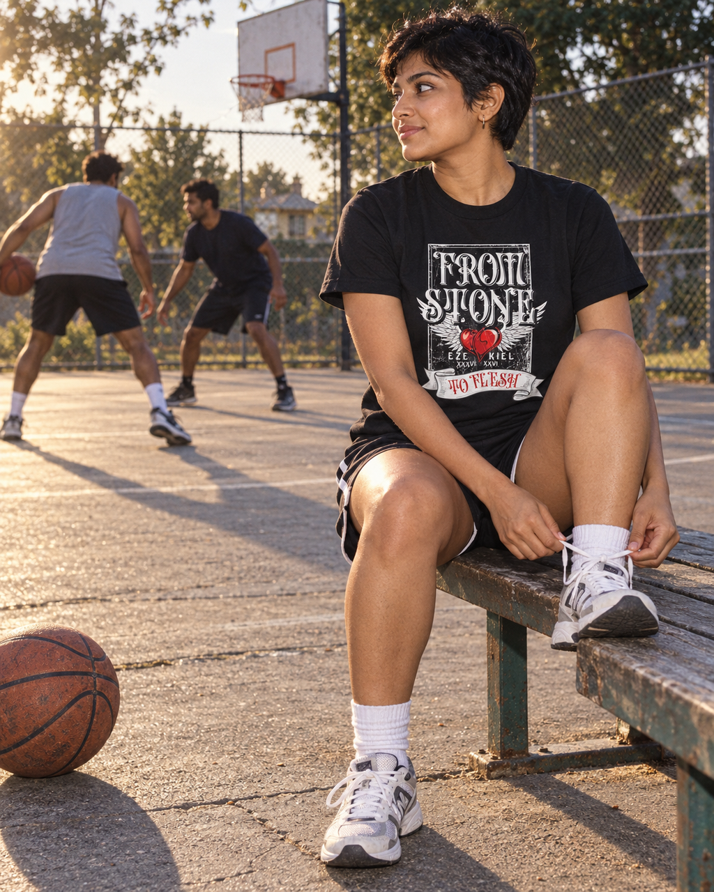 lifestyle mockup of an adult tying a shoe at a basketball court in the black Heart of Flesh tee, with its From Stone to Flesh front artwork visible.