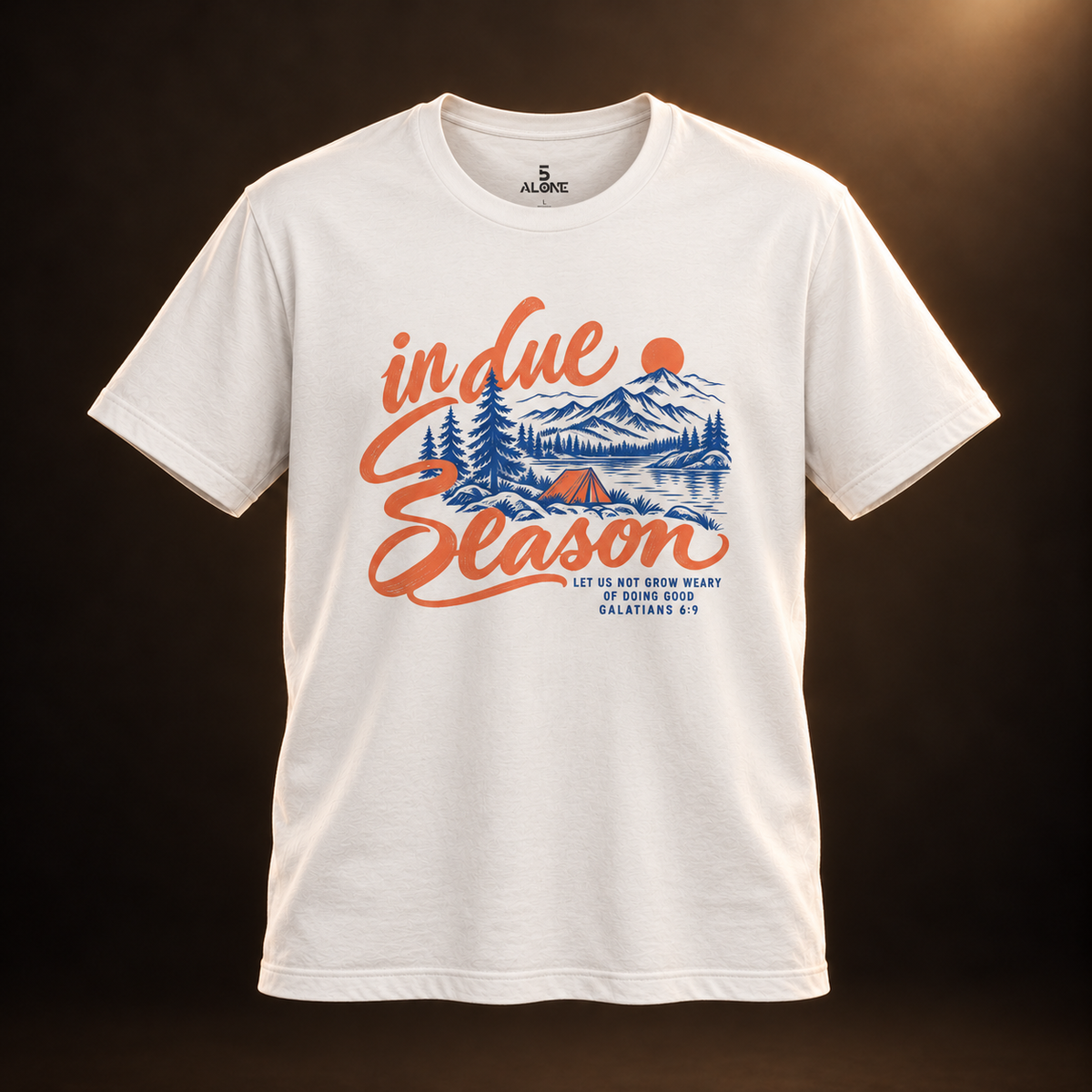 Front view of the Vintage White In Due Season tee with apricot lettering and blue mountain and camping artwork, lit in a warm dark studio.