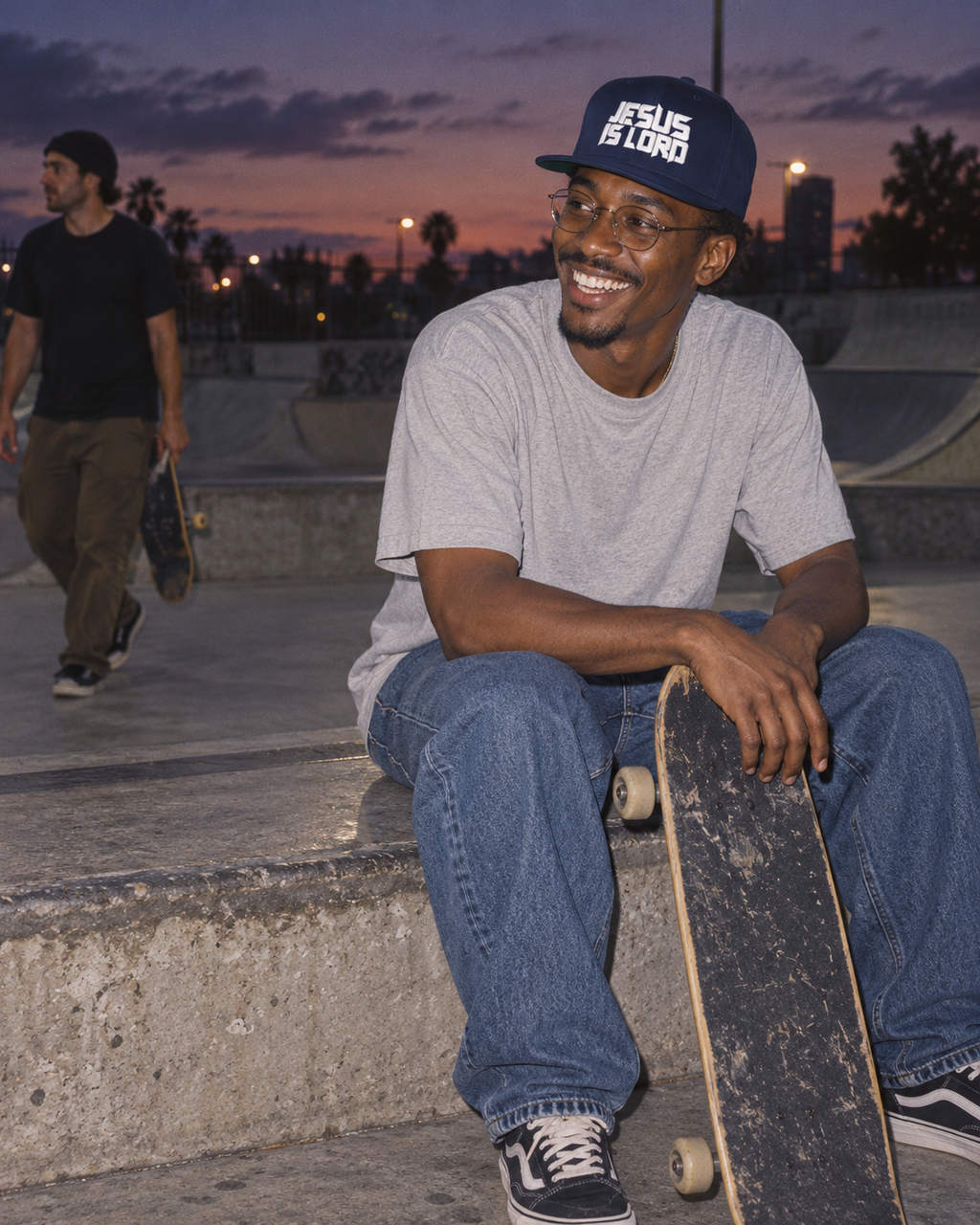 lifestyle mockup: adult wearing the navy Jesus Is Lord cap during a skatepark break at dusk; white front embroidery visible.