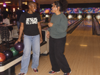 lifestyle mockup of an adult chatting with a friend beside a bowling ball return, wearing the black Jesus Is Lord tee with its cream front lettering visible.