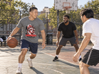 lifestyle mockup of an adult playing outdoor basketball in the Deep Heather Liberated tee, with its Statue of Liberty front artwork visible in a candid daylight scene.