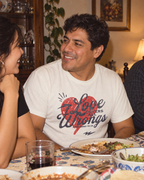 lifestyle mockup of a young adult enjoying dinner conversation with friends, wearing the vintage white Love Covers All Wrongs tee with its red heart and dark front lettering visible.