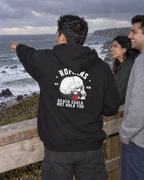 lifestyle mockup of young adult friends at a coastal overlook, with a man seen from behind in the black Romans Death hoodie showing the white skull, red rose and Death Could Not Hold You back artwork.