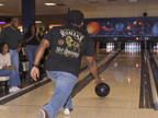 lifestyle mockup of an adult bowling with friends, photographed from behind in the black Romans Lion tee with its lion and Romans 1:16 back artwork visible.