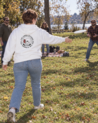lifestyle mockup of an adult playing frisbee with friends in a sunny park, seen from behind in the white Rose Skull hoodie with its circular skull, rose and Isaiah 40:8 back artwork visible.